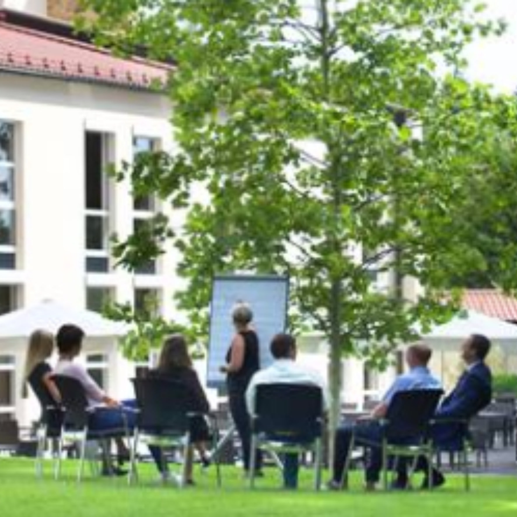 Tagungsrunde im Freien vor dem Haus, Flipchart zwischen den Bäumen