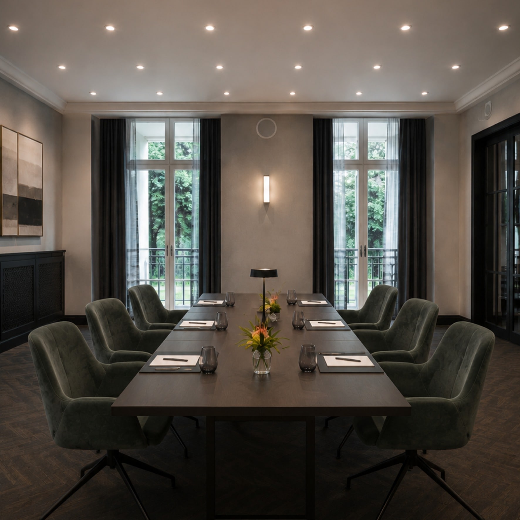 Das Kaminzimmer mit langem Tisch, grünen Polsterstühlen und hohen Fenstern