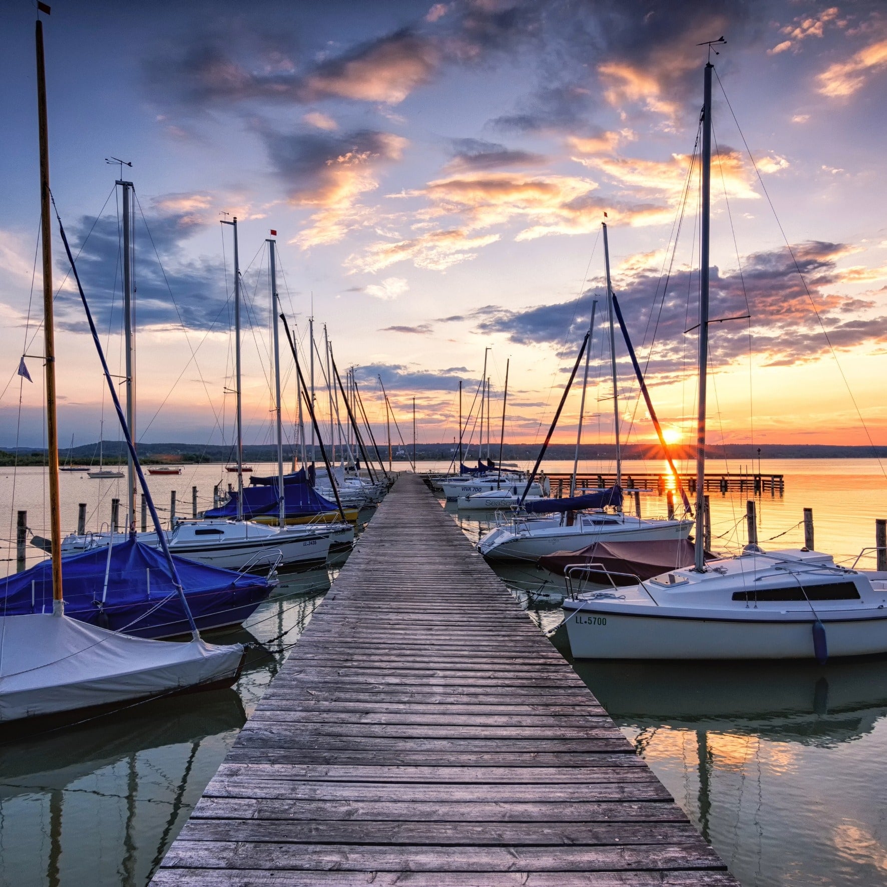 Bootssteg am Ammersee zwischen vertäuten Segelbooten bei Sonnenuntergang