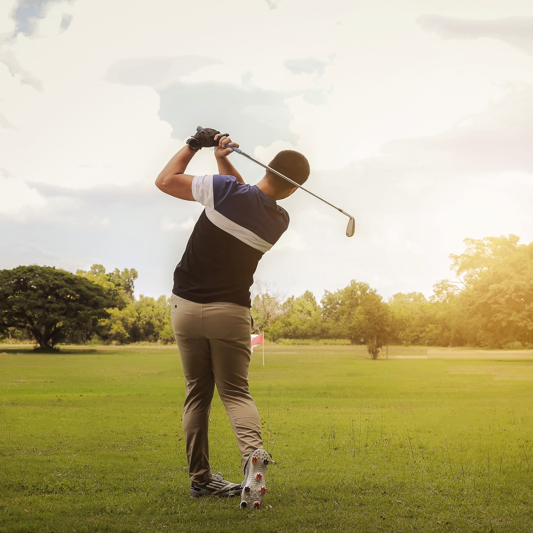 Golfspieler beim Abschlag auf weitem Fairway im Abendlicht